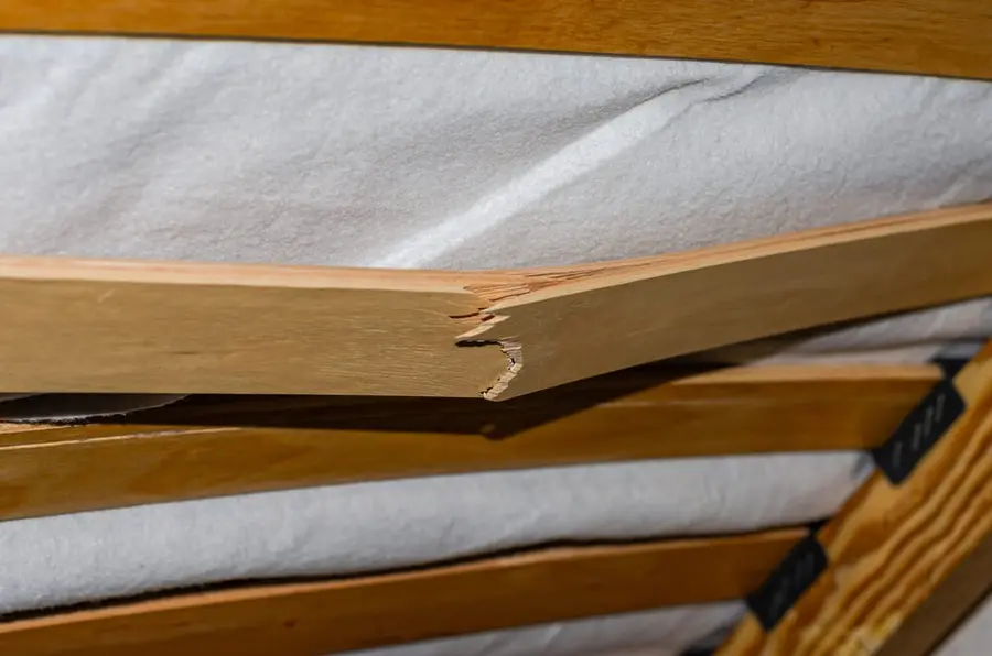 Detail prasklé dřevěné lamely roštu pod matrací.
