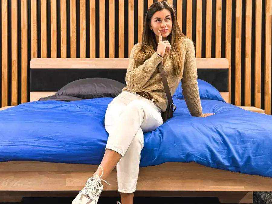 Žena sedí na kraji masivní postele v showroomu a přemýšlí nad výběrem.